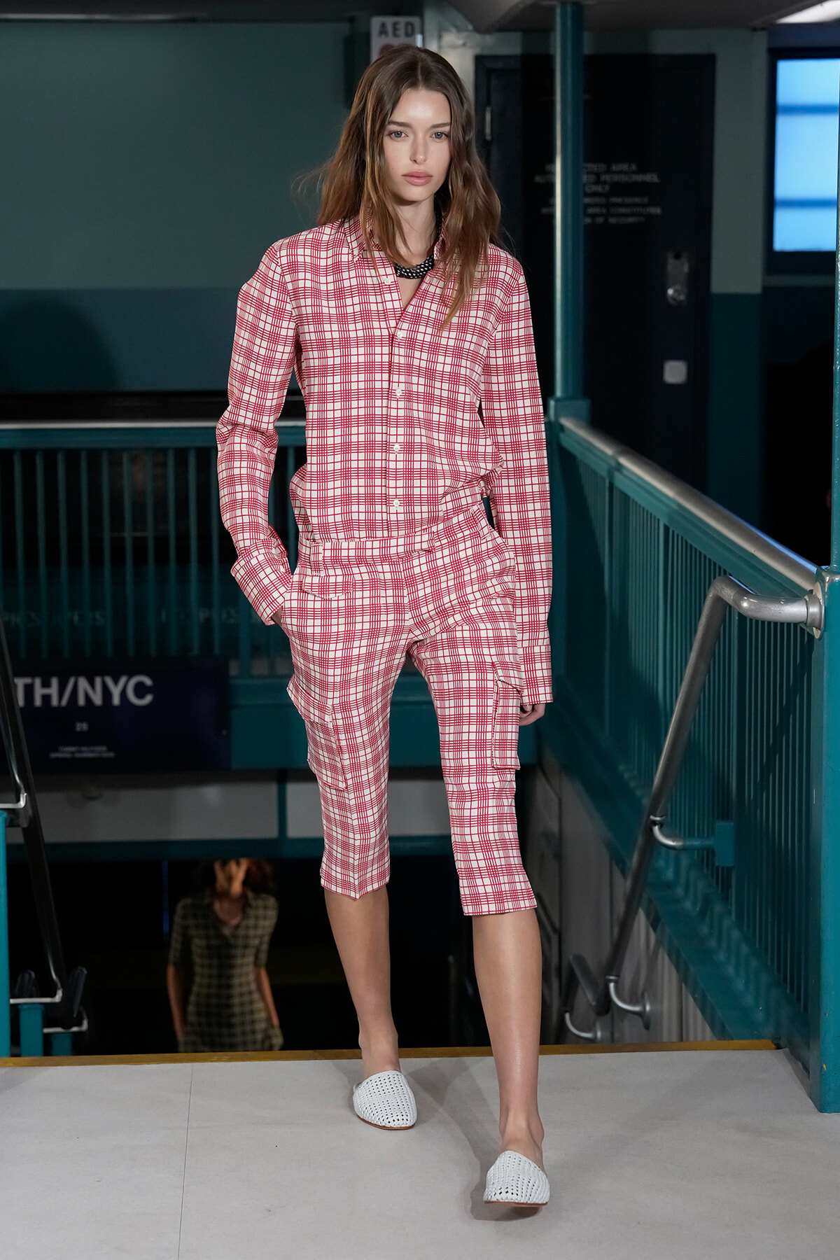 Model walking the runway in a pink plaid matching shirt and knee-length shorts, white woven slip-ons.