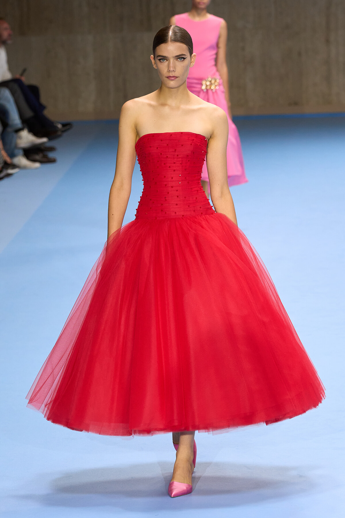 Model walking the runway in a strapless red ball gown with a full tulle skirt.