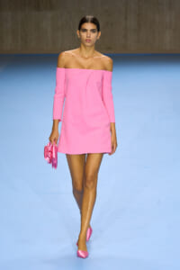 Model walking the runway in a pink off-shoulder mini dress with matching pink clutch and heels