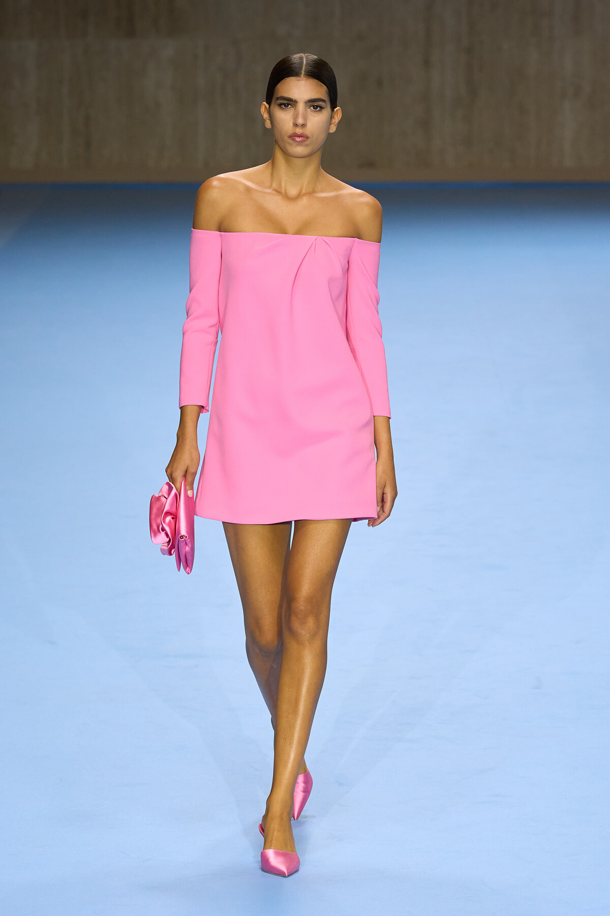 Model walking the runway in a pink off-shoulder mini dress with matching pink clutch and heels
