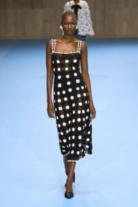 Model walks the runway in a black crochet midi dress with white polka-dot accents.