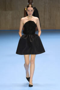 Model walking the runway in a strapless black sequin bodice and full satin mini skirt on a blue catwalk.