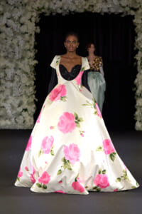 Model walks the runway in a cream ballgown with large pink rose prints and a black sequined sweetheart bodice.