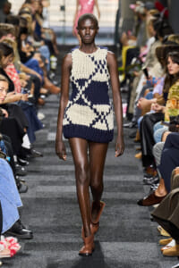 Model walks the runway in a navy and cream chunky knit sleeveless mini dress, paired with brown ankle boots.