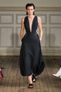 Model wears a black deep-V gown with pearl fringe details at the sides on a runway.