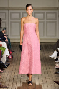 Model walking a runway in a strapless pink textured midi dress, black gloves, and black sandals.