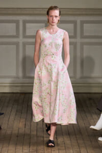 Model walking in a pink sleeveless midi dress with a white floral print on a wooden runway.