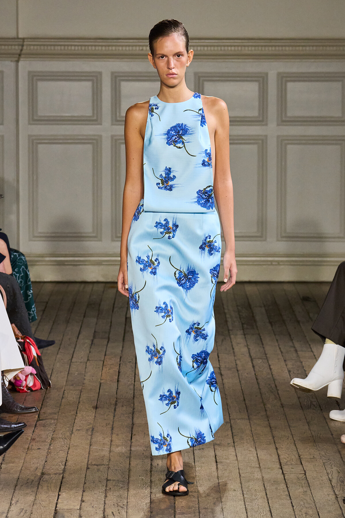 Model walking a light blue sleeveless floral halter-neck maxi dress on a runway.