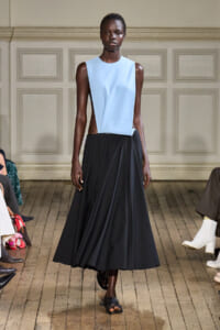 Model walks the runway in a light blue sleeveless top and a full-length black skirt.