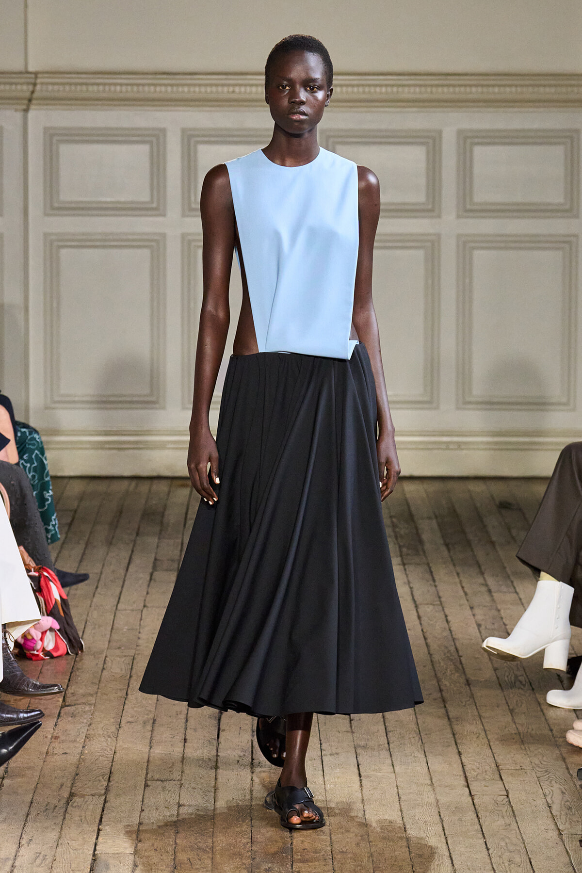 Model walks the runway in a light blue sleeveless top and a full-length black skirt.