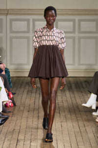 Model walks the runway in a two-tone dress: pink geometric patterned top with a brown flared skirt.