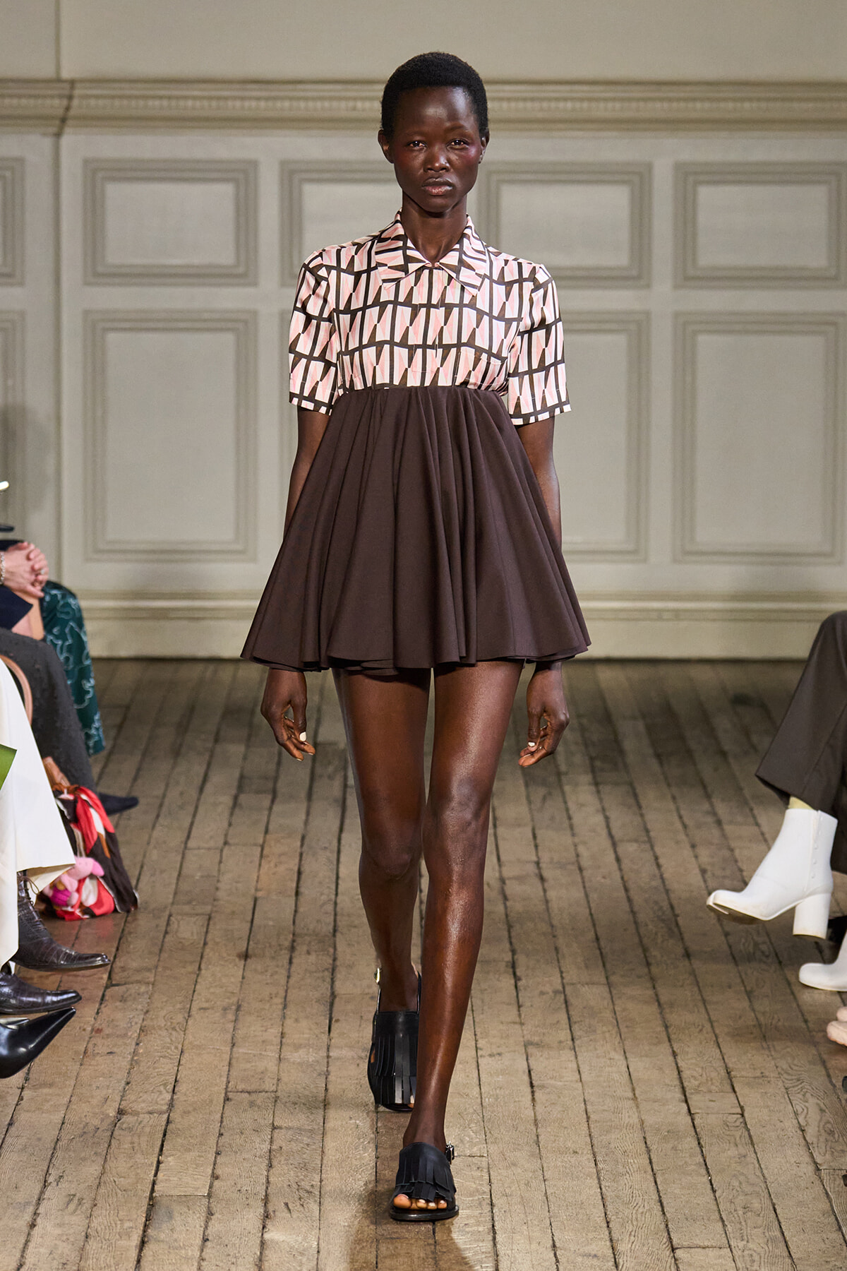 Model walks the runway in a two-tone dress: pink geometric patterned top with a brown flared skirt.