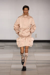 Model walking runway in a pale pink oversized windbreaker with drawstrings and matching shorts with large pockets and gathered hems due to a fashion-forward ensemble.