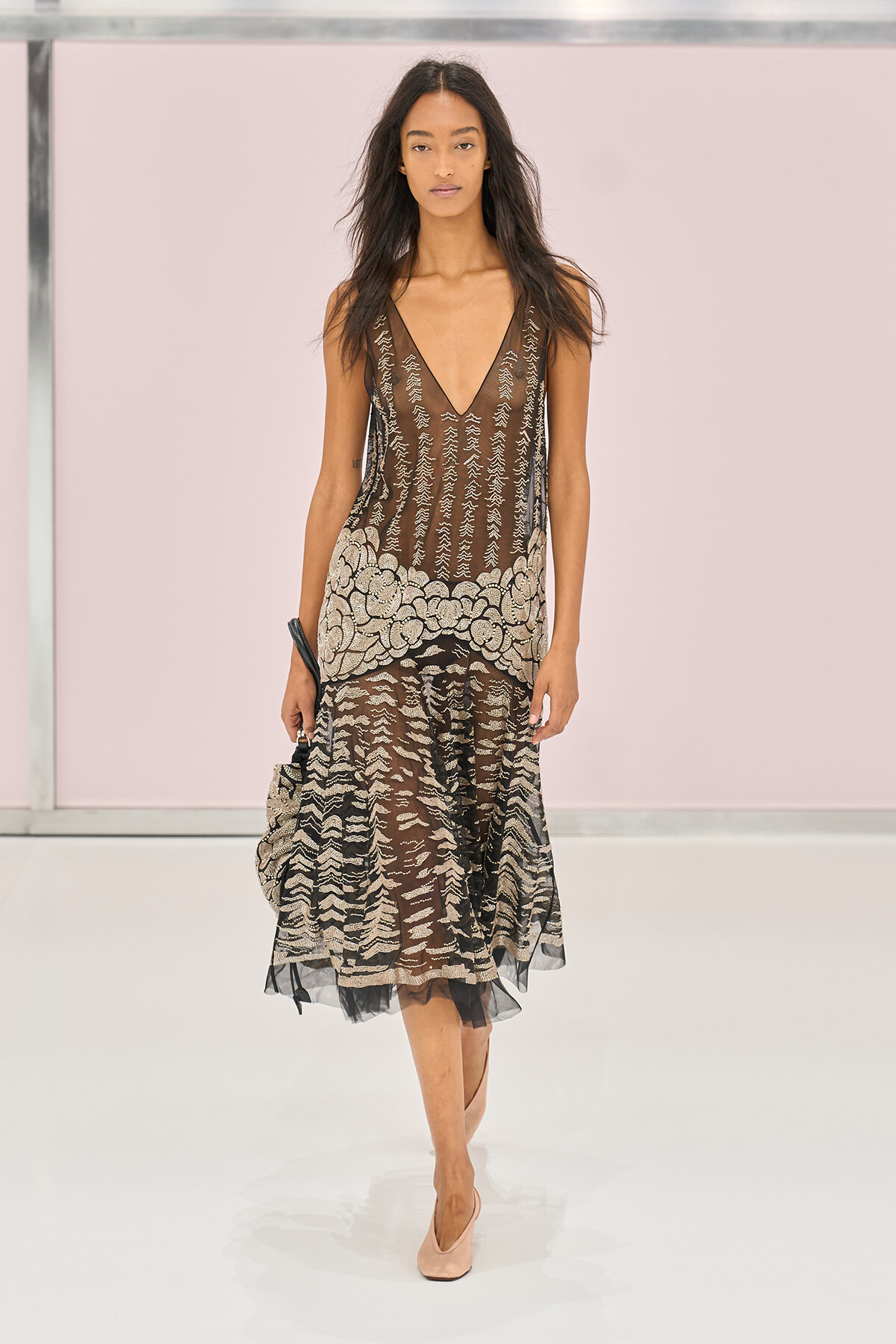 Runway model wearing a sheer brown and black lace dress with a floral-hem pattern and pale pink heels.