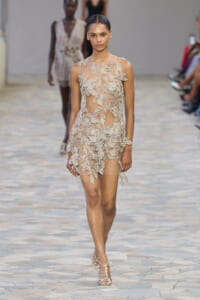 Model walks the runway in a sheer nude dress covered with white leaf lace appliqués.