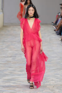 Model walks the runway in a hot pink sheer gown with a deep V-neck, layered ruffles, and a black jeweled choker at the fashion show.