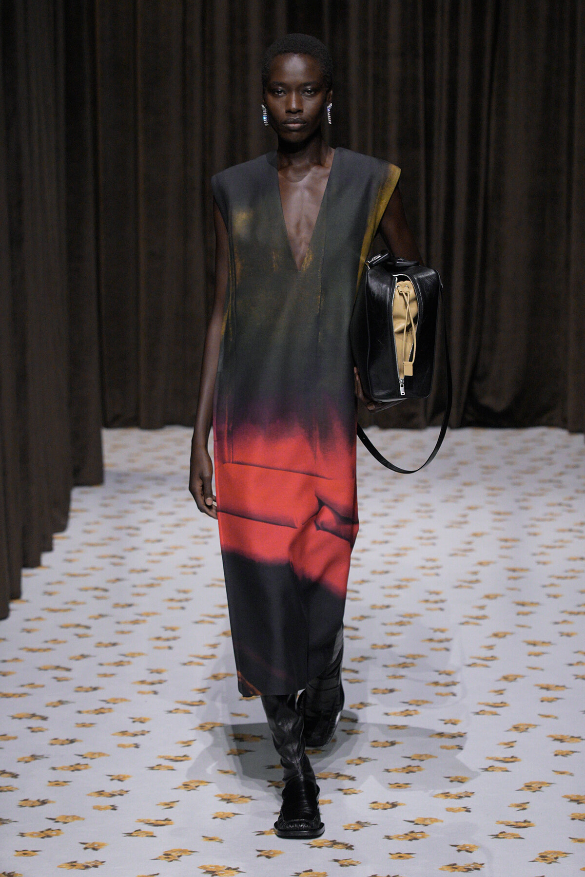 Model on runway wearing a sleeveless V-neck dress fading from dark green to red, with black boots and a black bag.