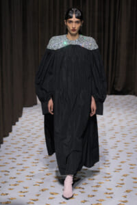 Model in a sweeping black gown with a sparkling silver embellished yoke and pale pink ankle boots on the runway.