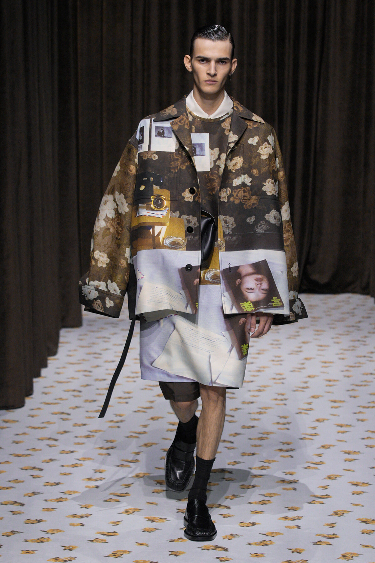 Male model walks the runway in a brown floral collage coat with photo-montage prints, white shirt, and black loafers.