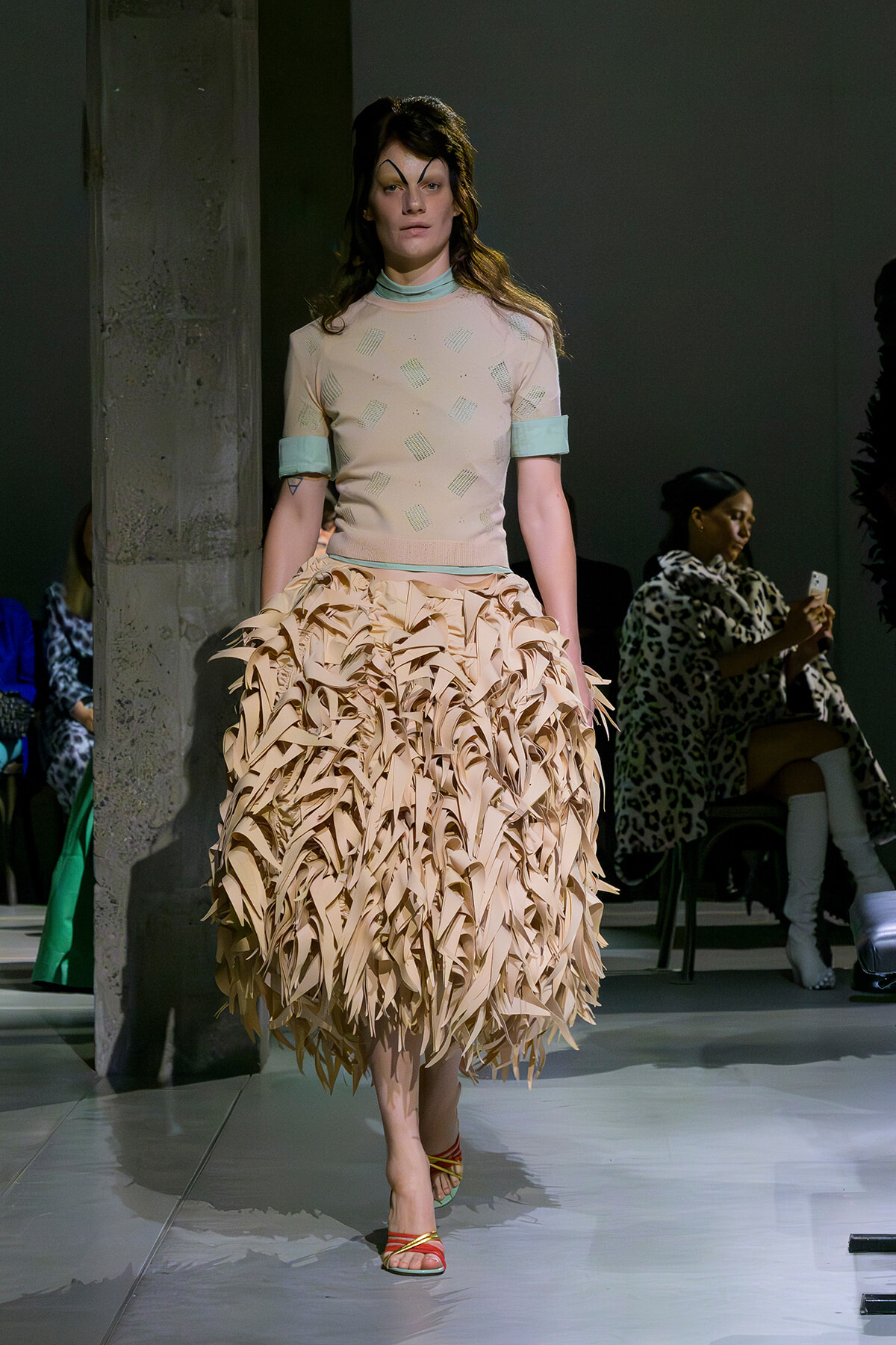 Model walks the runway in a pale pink top with mint cuffs and a voluminous beige ruffled skirt.