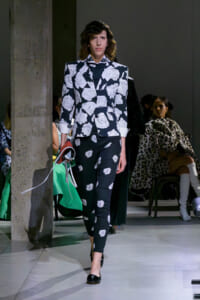 Model walks the runway in a black-and-white rose-print suit, blazer with rolled cuffs and matching pants.