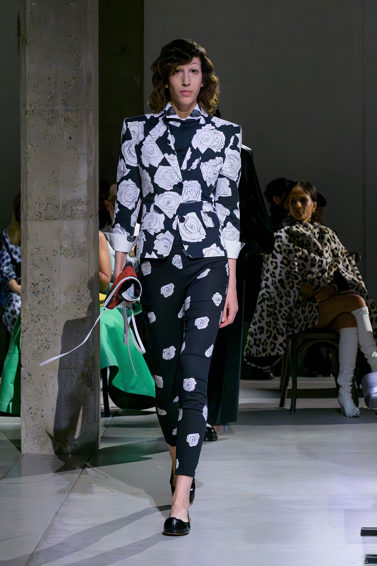 Model walks the runway in a black-and-white rose-print suit, blazer with rolled cuffs and matching pants.