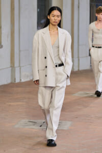 Model walking in a light beige oversized blazer and matching wide-leg suit, neutral top, black belt, black shoes on a brick runway.