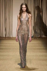 Model on a runway wearing a long, glittering halter-neck gown covered in sequins.