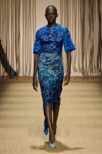 Model walks the runway in a blue crinkled fabric dress with short puff sleeves and an asymmetric hem.