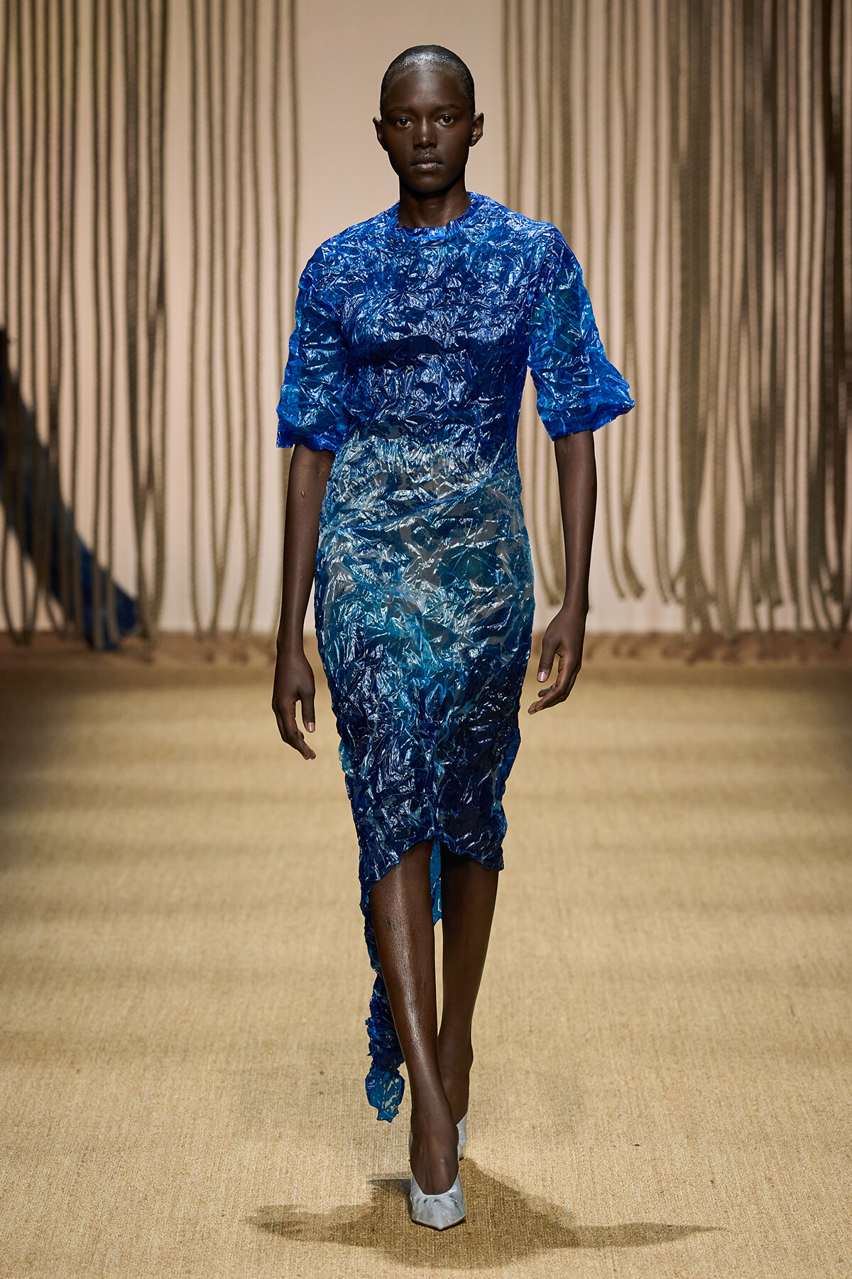 Model walks the runway in a blue crinkled fabric dress with short puff sleeves and an asymmetric hem.