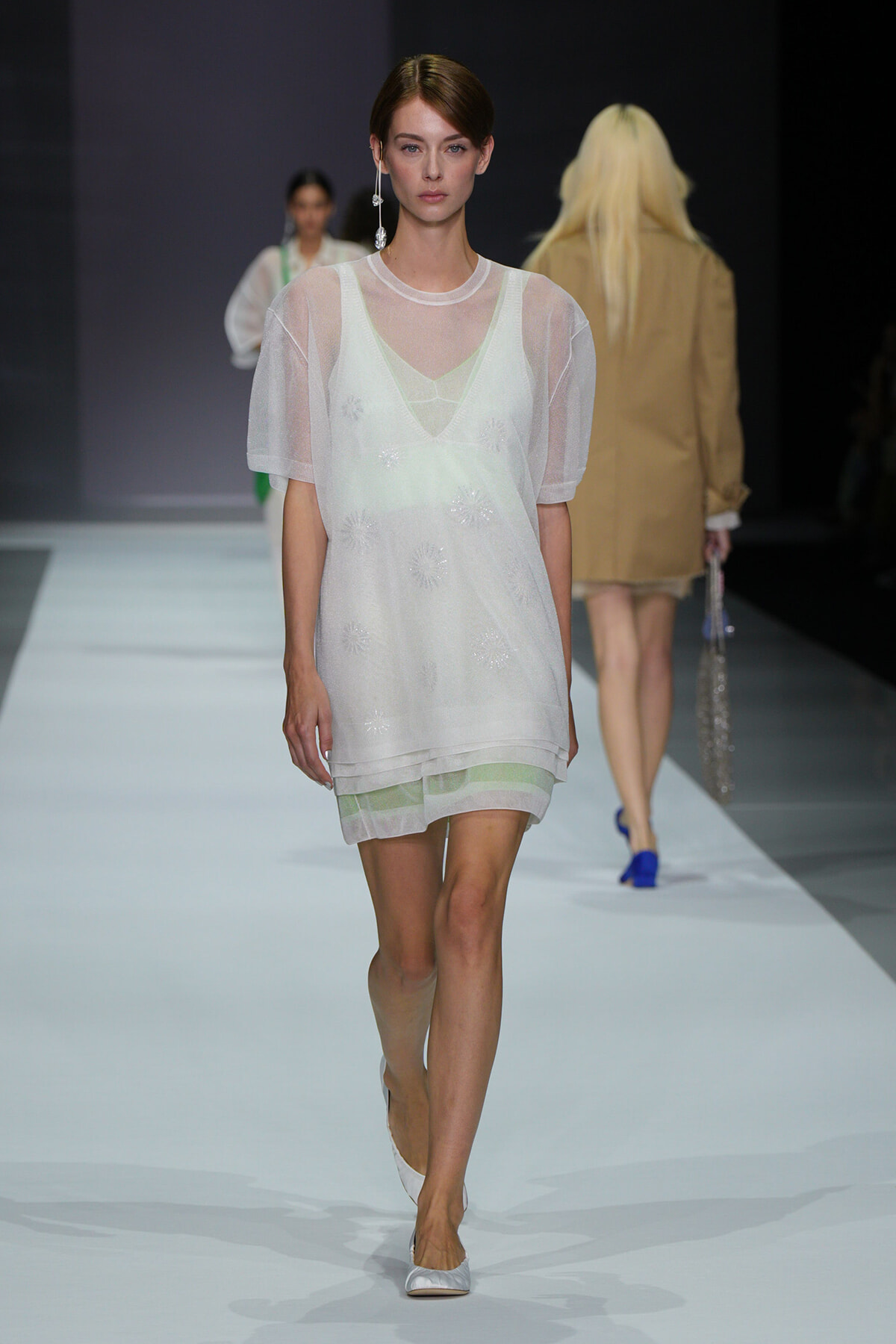 Model walks the runway in a white sheer layered dress with a pale green underlayer and white flats.