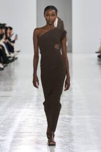 Model walks the runway in a one-shoulder, ribbed brown knit dress with a side cutout.