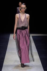 Model walks the runway in a pink beaded halter top with a black belt and a layered pink skirt topped with black tulle, wearing sunglasses and hoop earrings.