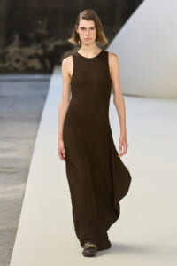 Model walking a fashion runway in a sleeveless dark brown maxi dress.
