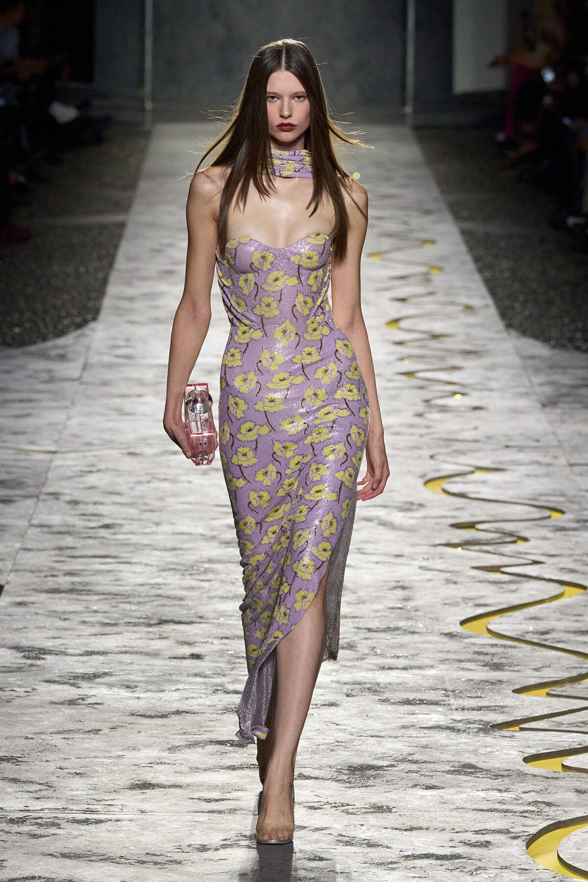 Slim model walking a runway in a lavender floral strapless dress with a matching choker and pink clutch.