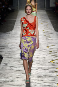 Runway look: red satin draped top with green embroidery paired with a lavender floral-print wrap skirt on a model.