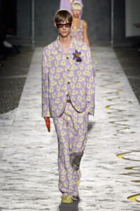 Model walking the runway in a lavender floral suit with matching pants and oversized sunglasses.
