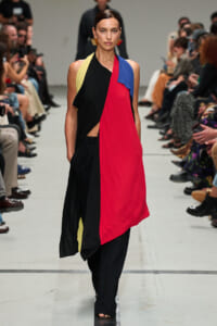 Model walks a runway wearing a color-blocked sleeveless dress with red, black, yellow, and blue panels.