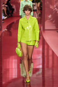 Model walks a fashion show in a neon lime-green leather suit with gloves and a matching handbag.