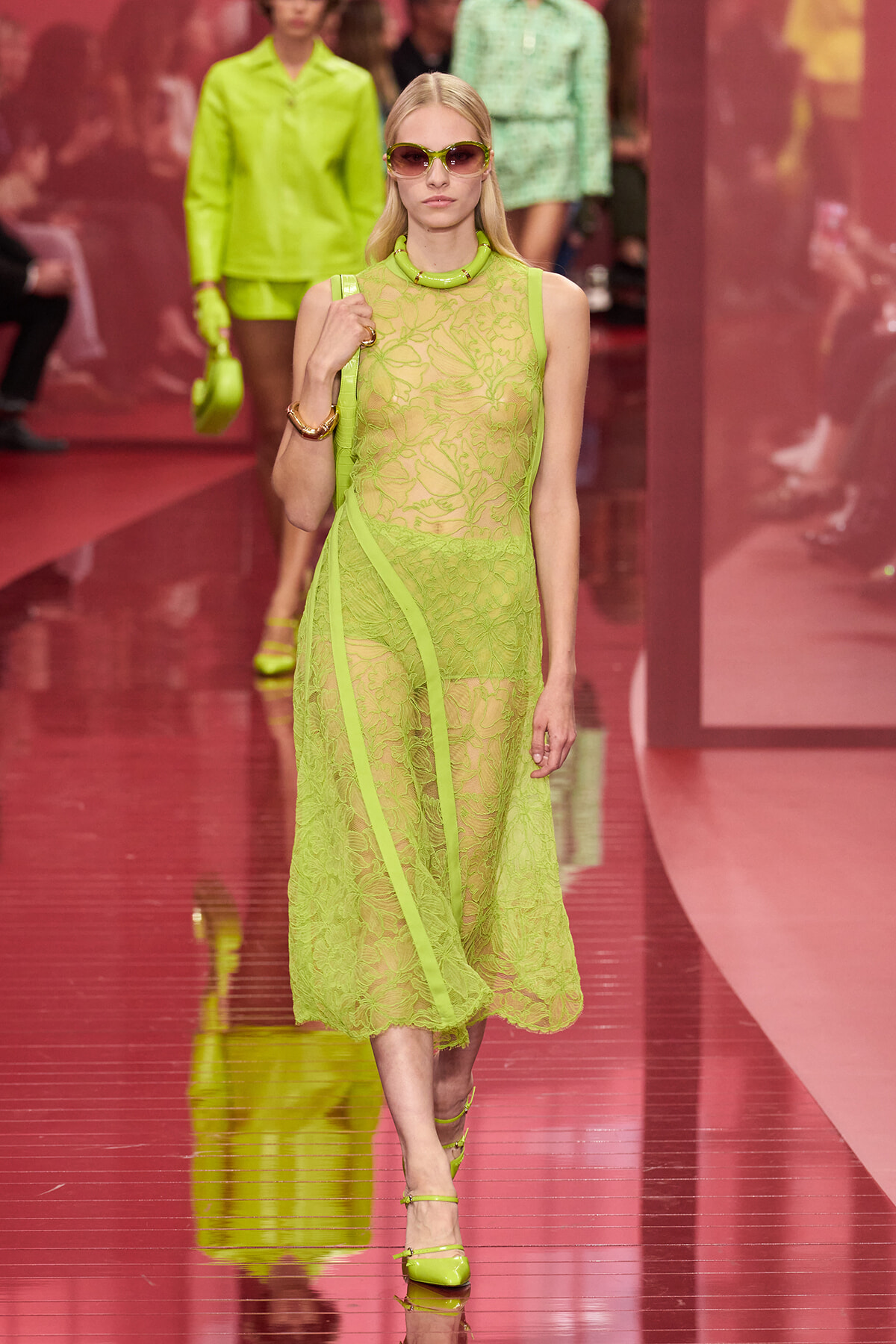 Model walks a neon-green lace ensemble down a runway, accessorized with matching sunglasses and heels.