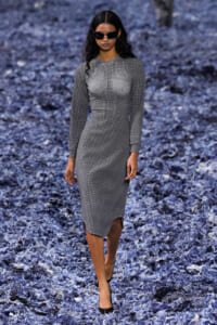 Model walks the runway in a gray plaid long-sleeve midi dress, black sunglasses, and black heels.