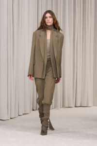 Model wearing a taupe oversized blazer with matching pants and scrunched ankles on a runway.