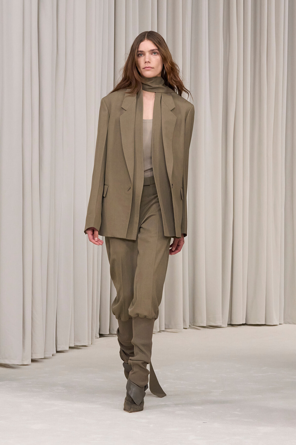 Model wearing a taupe oversized blazer with matching pants and scrunched ankles on a runway.