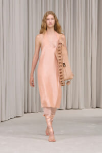 Model walking the runway in a pale pink, sequined slip dress with a matching oversized bag slung over the shoulder.