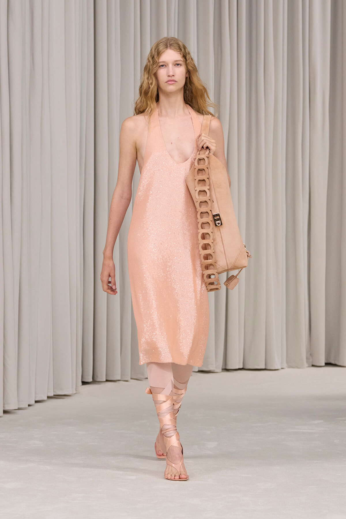 Model walking the runway in a pale pink, sequined slip dress with a matching oversized bag slung over the shoulder.