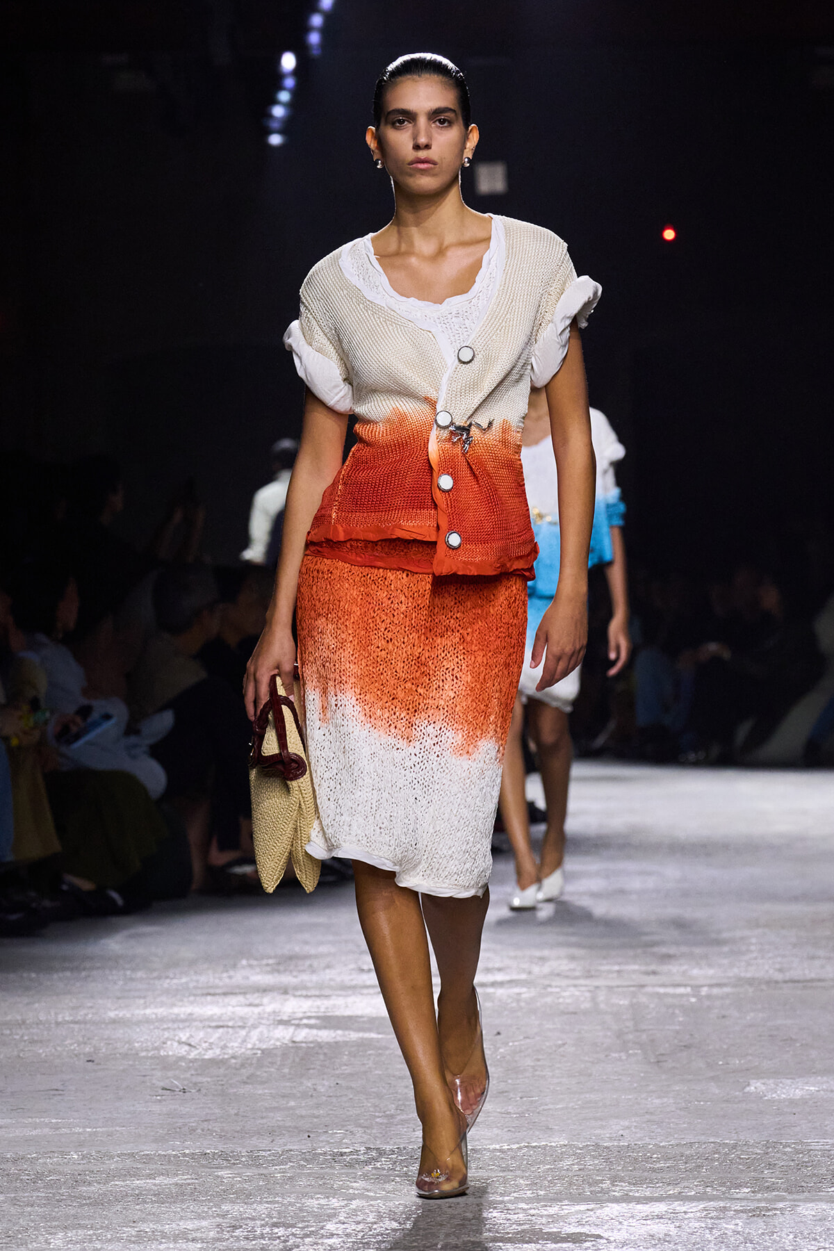Model walks the runway in a cream-to-orange gradient knit dress with rolled sleeves, carrying a straw handbag.