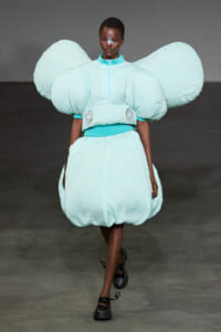 Model wearing a futuristic light-blue sculptural outfit with oversized shoulder puffs and a bubble skirt on a runway.
