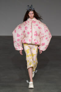 Model walks the runway in a voluminous pale pink polka-dot puffer jacket with matching pants and a metallic crown headpiece.