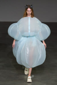 Model walks the runway in an oversized pale blue bubble dress with voluminous sleeves and a sculptural headpiece.