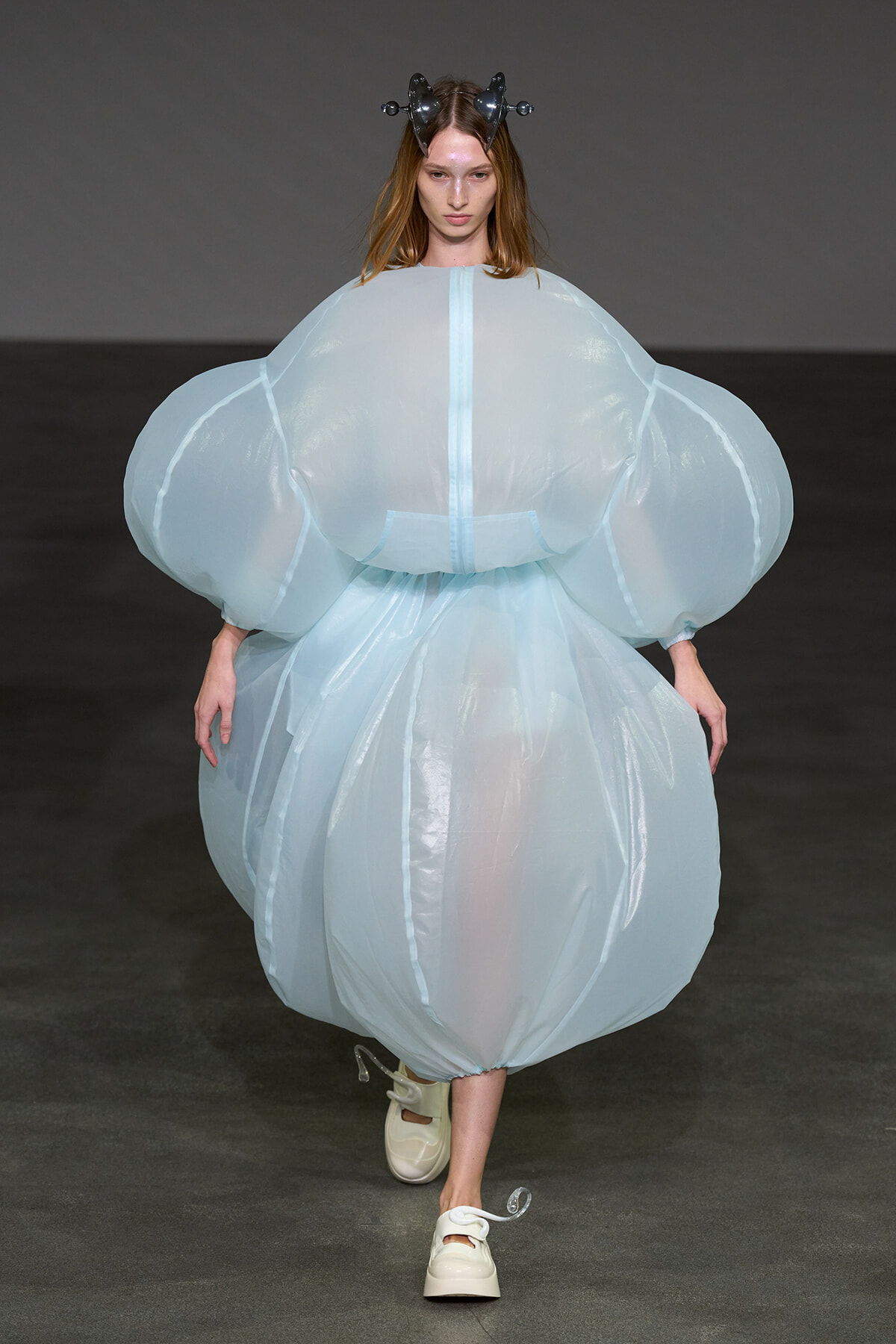 Model walks the runway in an oversized pale blue bubble dress with voluminous sleeves and a sculptural headpiece.